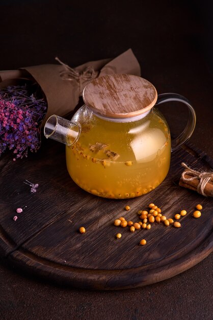 Tè caldo con l'olivello spinoso in teiera di vetro, fuoco selettivo, fondo rustico