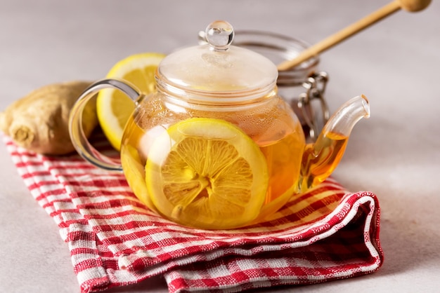 Tè caldo con limone in teiera su tovagliolo di lino Teiera in vetro con bevanda sana per raffreddore e influenza