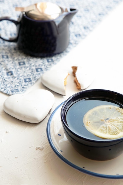 Tè caldo con una fetta di limone fresco alla tazza da tè blu con cuori di biscotti. cibo delizioso gustoso. teiera blu e tovagliolo blu