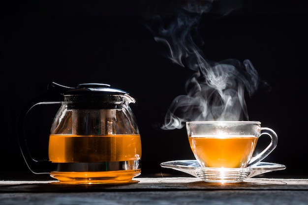 Tè caldo in teiera e tazza di vetro con vapore su fondo di legno
