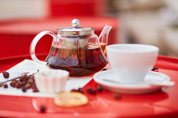 Tè caldo in teiera e tazza di vetro, su sfondo rosso