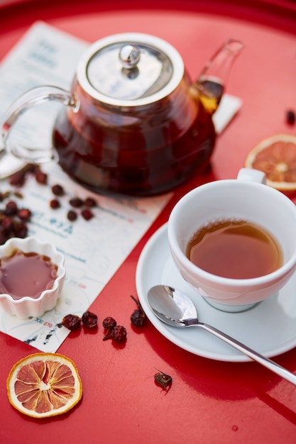 Tè caldo in teiera e tazza di vetro, su sfondo rosso