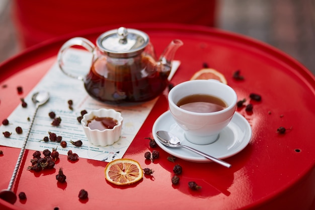 Tè caldo in teiera e tazza di vetro, su sfondo rosso