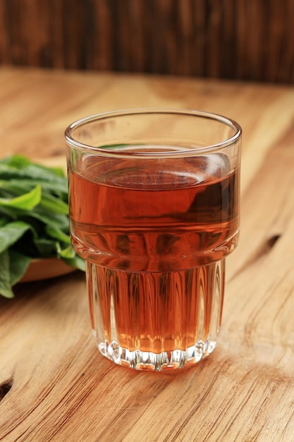 Tè caldo in un bicchiere con sfondo di foglie di tè fresche