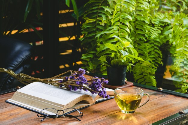 Tè caldo in una tazza con il libro aperto e occhiali da lettura con fiori secchi sul tavolo