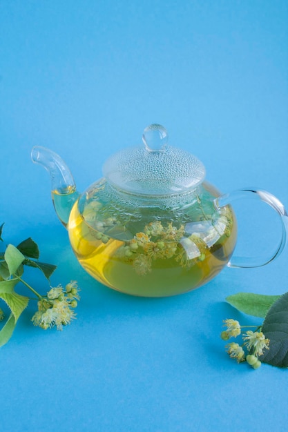 Tè con fiori di tiglio nella teiera di vetro su sfondo blu Closeup Posizione verticale