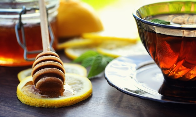 Tè con limone e menta in natura. Una tazza di tè caldo alla menta con limone e miele in barattolo. Fette di limone e un cucchiaio con miele per il tè caldo.