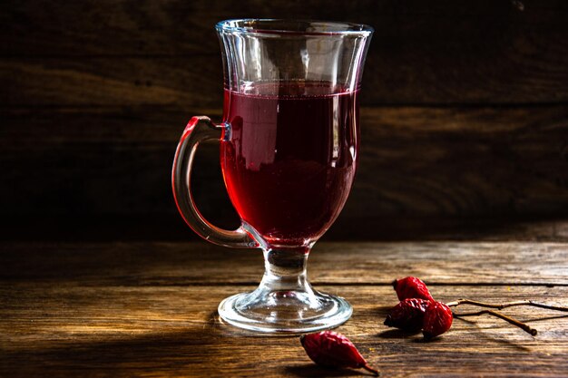 Tè di rosa canina in una tazza di vetro su uno sfondo di legno.