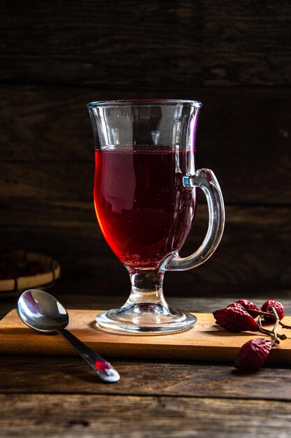 Tè di rosa canina in una tazza di vetro su uno sfondo di legno.