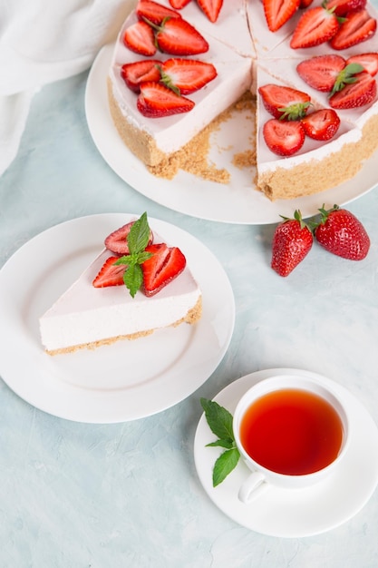 Tè dolce per la colazione e deliziosa torta di formaggio con fragole fresche e menta ricetta fatta in casa senza cottura su un tavolo di pietra blu Copia spazio