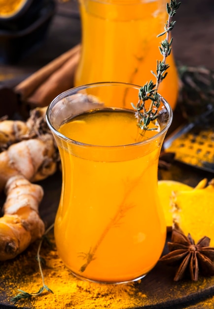 Tè dorato alla curcuma vegano sano con miele in tazza di vetro su vassoio di legno Tè speziato curativo alle erbe