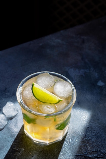 Tè freddo con cubetti di ghiaccio foglie di menta lime nel bicchiere su sfondo di pietra grigia