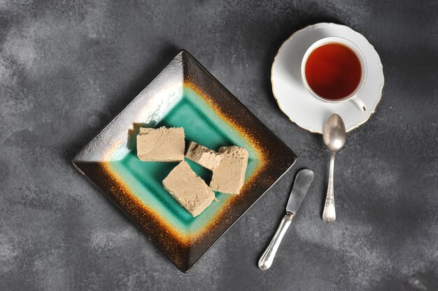 Tè in una tazza con un bordo dorato e un piattino e halva tagliati a pezzi