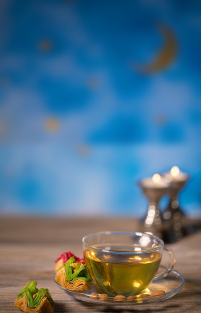 Tè in una tazza di vetro con dolci arabi su una superficie di legno Cielo blu notte sullo sfondo