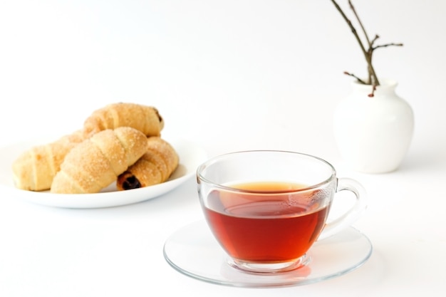 Tè in una tazza trasparente e croissant fatti in casa con marmellata e una pianta isolata su sfondo bianco