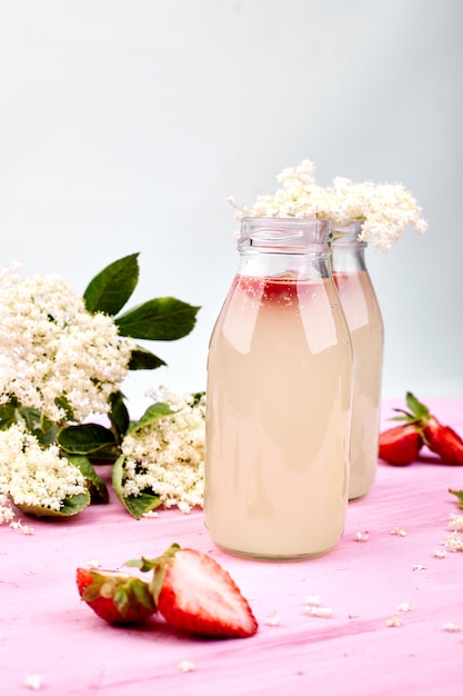 Tè Kombucha con fiori di sambuco e fragola su sfondo rosa.