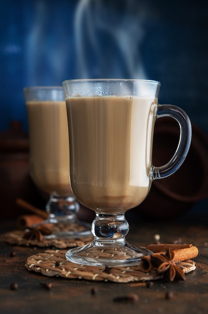 Tè Masala con cannella e badian su un tavolo di argilla. Due bicchieri di tè masala su sfondo blu.