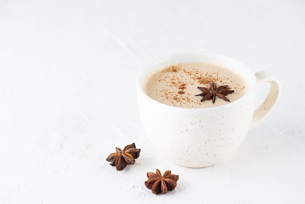 Tè masala fatto in casa con latte, radice di zenzero e spezie in una tazza sul tavolo. Senza lattosio, vegan.