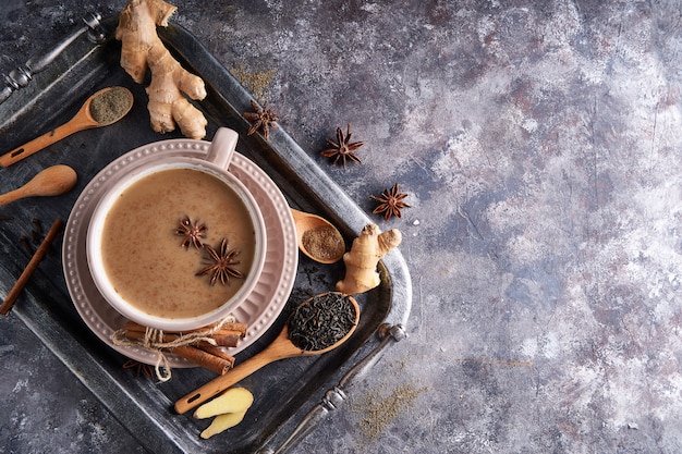 Tè Masala in tazza con spezie zenzero, cannella, anice, pepe nero sul tavolo grigio sone