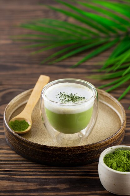 Tè Matcha latte con latte di cocco e semi di canapa in un bicchiere sullo sfondo di un ramo di palma.