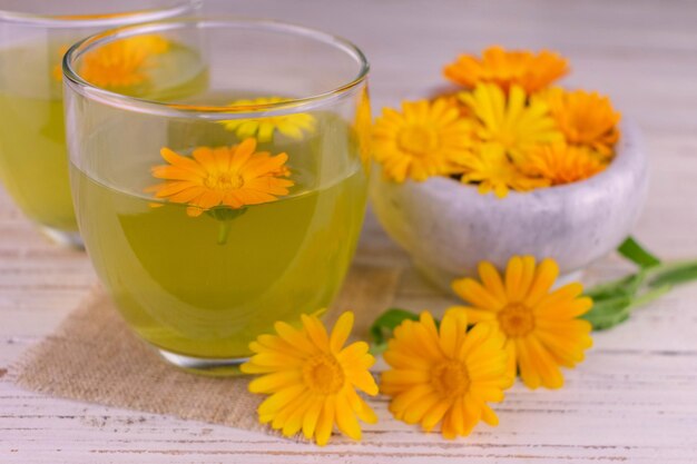 Tè medicinale con calendula in bicchieri su sfondo bianco.