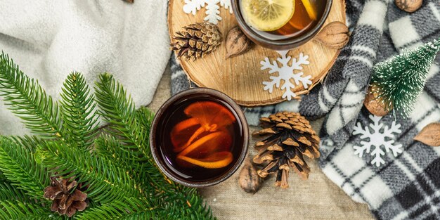 Tè nero caldo e limone con decorazioni invernali. Maglione accogliente, rami di abete, noci, fiocchi di neve. Disposizione festiva stagionale, concetto di buon umore, stile rustico, formato banner