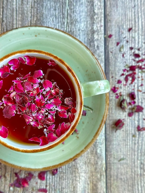 Tè nero con petali di rosa in una tazza di porcellana su uno sfondo di legno, una bella tazza di tè floreale