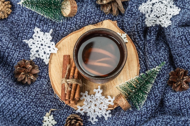 Tè nero in tazza di ceramica con decorazione tradizionale di Capodanno. Abeti, fiocchi di neve all'uncinetto, cannella e pigne. Supporto in legno, accogliente disposizione maglione lavorato a maglia, vista dall'alto