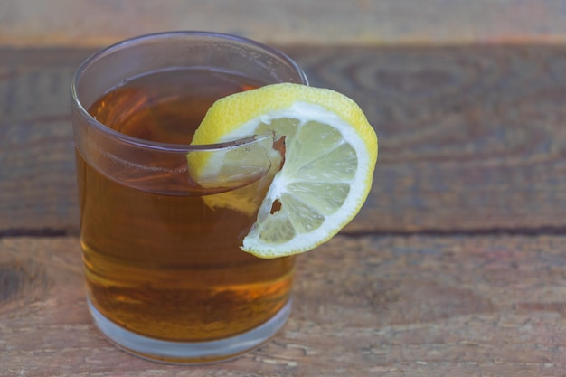 Tè nero in un bicchiere con una fetta di limone Concetto di benefici del tè con succo di limone su sfondo di legno