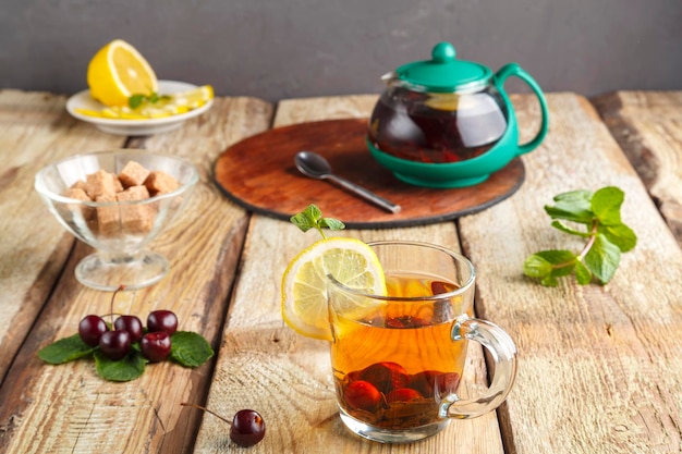 Tè nero in una tazza di vetro con ciliegie alla menta e limone su un tavolo di legno accanto a ciliegie fresche