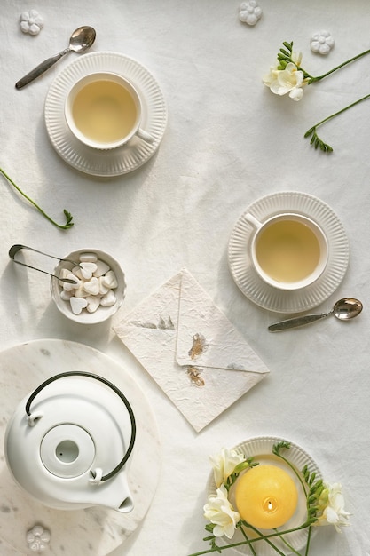 Tè pomeridiano primaverile Fiori di fresia primaverile teiera e tazza da tè sul tavolo Tovaglia tessile bianca piatta Uova di Pasqua tazze in ceramica bianca e cuori di zucchero