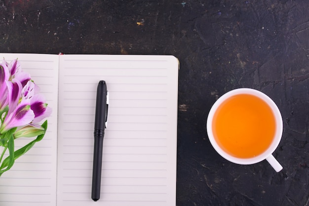 Tè profumato in una tazza bianca, bellissimi fiori, un quaderno con penna e occhiali.