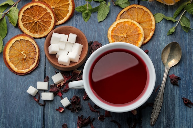 Tè rosso caldo karkade con miele e menta su un tavolo di legno blu.