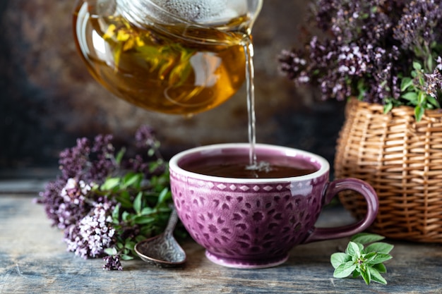 Tè sano dall'origano fiorisce in una bella tazza su una superficie di legno