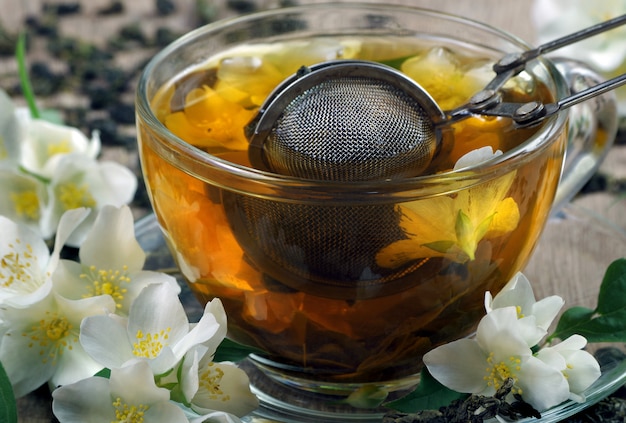 tè verde al gelsomino. foglie di tè verde secco con fiori di gelsomino e una tazza di tè su un tavolo di legno.