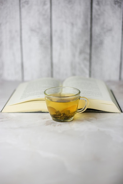 Tè verde alle erbe preparato in una tazza trasparente davanti a un libro aperto su sfondo chiaro