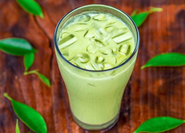 Tè verde freddo matcha latte con latte in un bicchiere con ghiaccio su legno