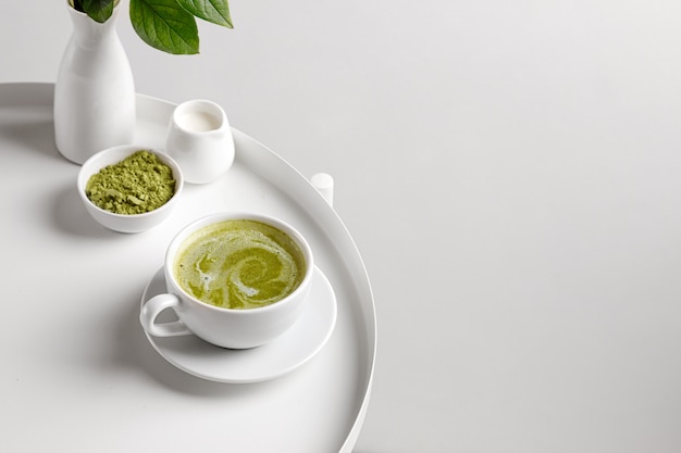 Tè verde matcha con latte in tazza sul tavolo bianco e backgriund bianco