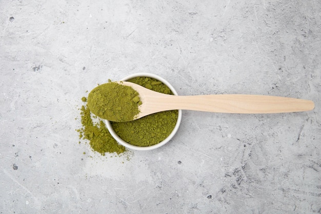 tè verde matcha in polvere in un cucchiaio di legno su un tavolo grigio