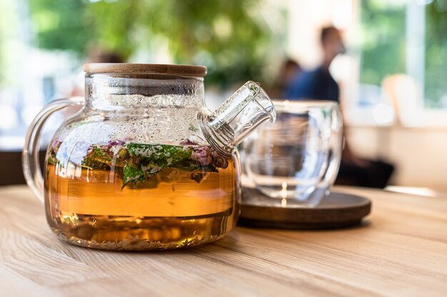 Tè verde o alle erbe in teiera di vetro con petali di menta e rose sul tavolo di legno al bar