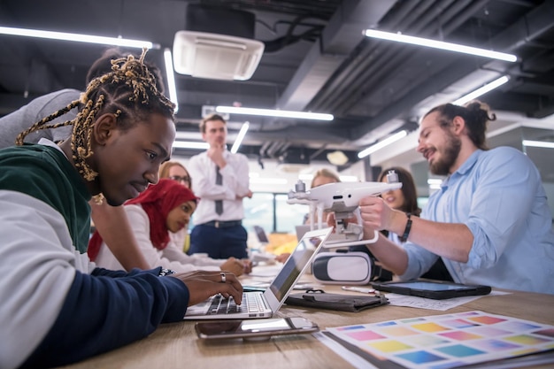 team aziendale di avvio multietnico che discute di un nuovo piano aziendale, lavora su laptop e tablet mentre apprende la tecnologia dei droni per il nuovo avanzamento del business