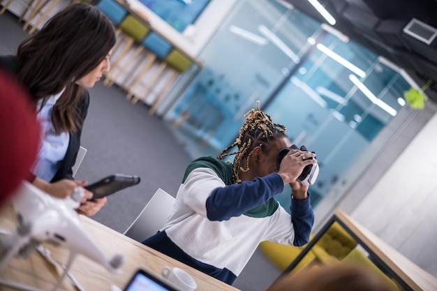 Team aziendale multietnico che utilizza cuffie per realtà virtuale in riunioni d'ufficio Gli sviluppatori si incontrano con un simulatore di realtà virtuale attorno al tavolo in un ufficio creativo.