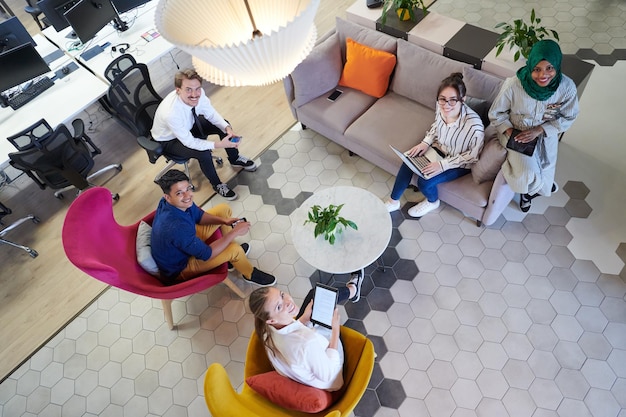 Team aziendale multietnico di avvio con brainstorming nell'area relax di interni di uffici moderni che lavorano su laptop e tablet