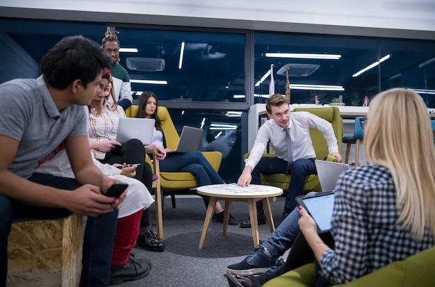 Team aziendale multietnico di avvio in riunione in un moderno e luminoso ufficio di brainstorming, lavorando su laptop e tablet