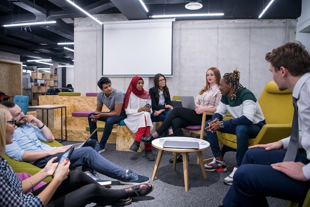 Team aziendale multietnico di avvio in riunione in un moderno e luminoso ufficio di brainstorming, lavorando su laptop e tablet