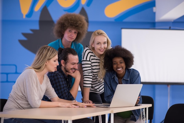 Team aziendale multietnico di avvio in riunione in un moderno e luminoso ufficio di brainstorming, lavorando su laptop e tablet