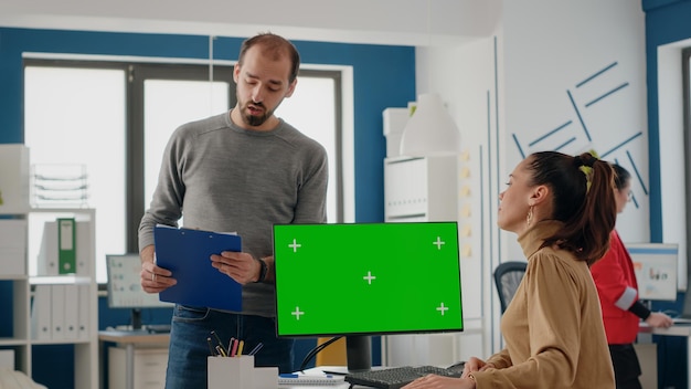 Team di colleghi che lavorano con lo schermo verde sul computer per il business di avvio. Uomo e donna che parlano mentre utilizzano un modello di mockup isolato con spazio di copia chiave cromatica sul monitor.