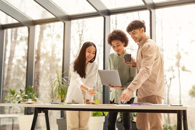 Team di colleghi diversi che svolgono un lavoro di squadra produttivo utilizzando il laptop in ufficio