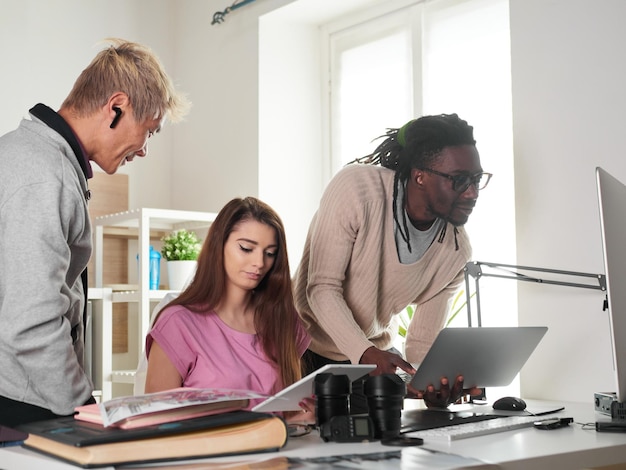 Team di fotografi che lavorano con un laptop sul posto di lavoro con due computer in studio