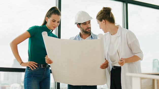 Team di ingegneri architetti professionisti che parlano condividono brainstorming sulla progettazione mentre il manager tiene il piano del progetto Il giovane architetto tiene il piano mentre il manager ascolta e indica il piano Tracery